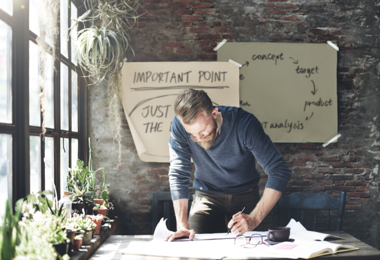 A bearded guy writes a text on a piece of paper. The title of the text says "starting your forex broker"