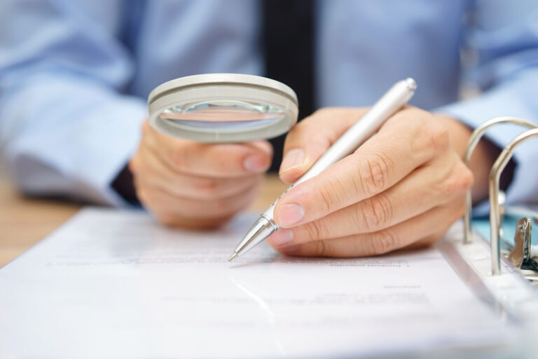 A business man with a magnifying glass carefully studies a piece of paper.